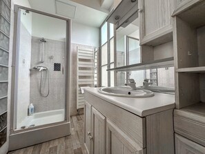 A modern bathroom with a glass-enclosed shower, a sink with a mirror above, and wooden cabinetry.