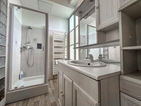 A modern bathroom with a glass-enclosed shower, a sink with a mirror above, and wooden cabinetry.