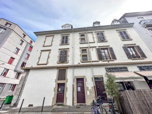 A multi-story building with a ground-level entrance, a door with a sign, and a window with shutters.