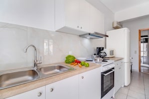 Une cuisine moderne dotée d’un évier en acier inoxydable, de meubles blancs, d’une cuisinière et d’un four à micro-ondes.