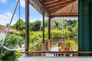 A balcony with a table and chairs, a view of a vineyard, and a building with green siding. - Apartment "Nikoleta 2" with Sea View, Terrace & Wi-Fi (Lefkada)
