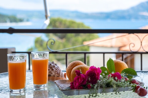 A table with two glasses of orange juice, a plate with bread, strawberries, and flowers, and a scenic view in the background. - Apartment 'Nikoleta 2' with Sea View, Wi-Fi and Air Conditioning (Lefkada)