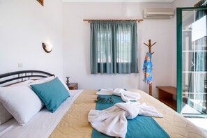 Hotelkamer met een bed, een raam met gordijnen, een wandairconditioner en een houten kapstok met een handdoek.