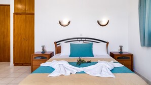 Een netjes opgemaakt bed met een blauw kussen, twee nachtkastjes met lampen, een houten garderobe en een wandlamp.