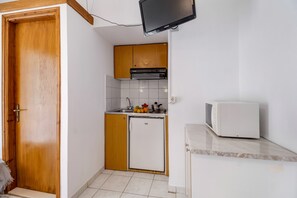 A compact kitchen with wooden cabinets, a white refrigerator, a microwave, and a flat-screen TV mounted on the wall.