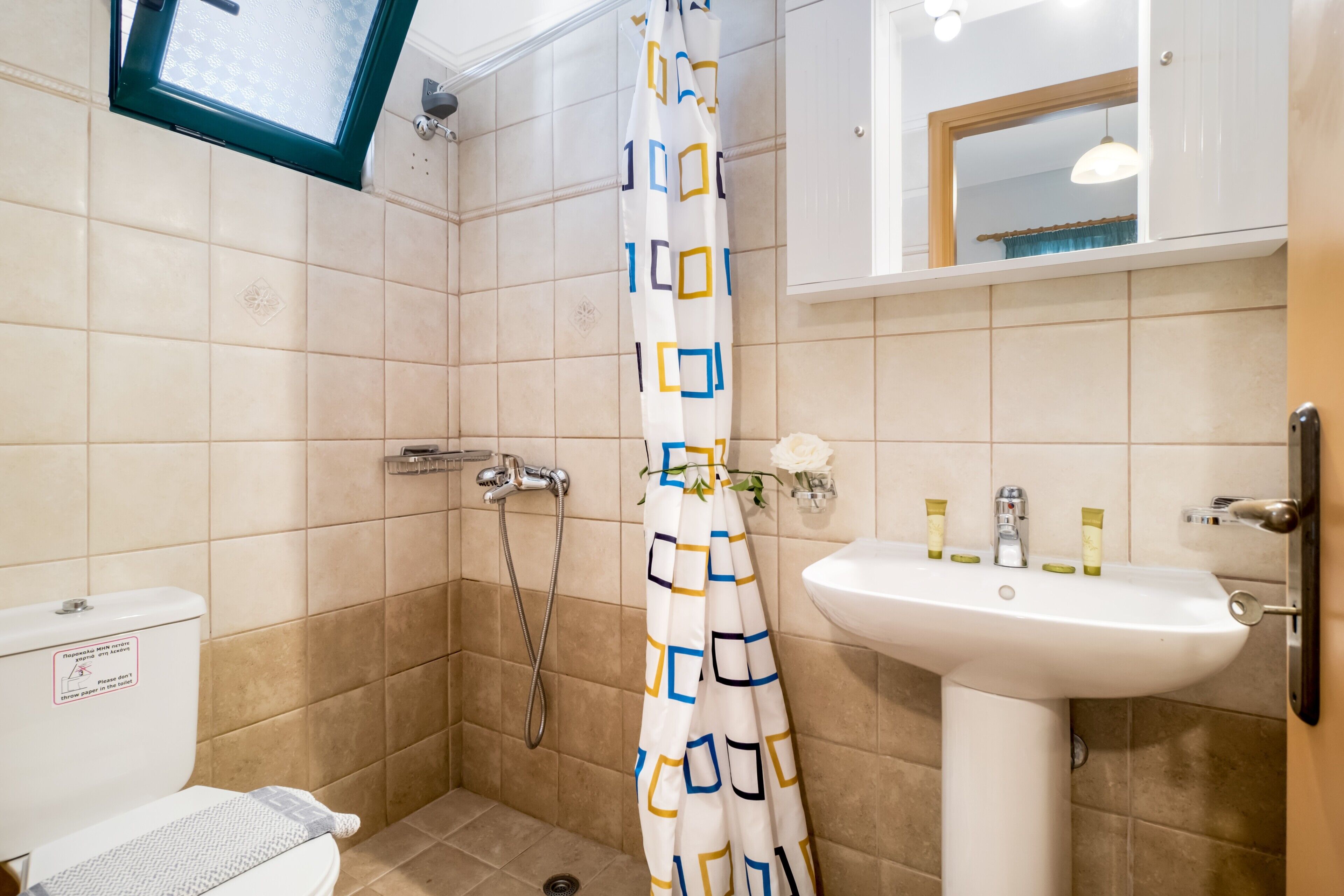 Un bagno con doccia, WC, lavandino e una finestra sopra la doccia.