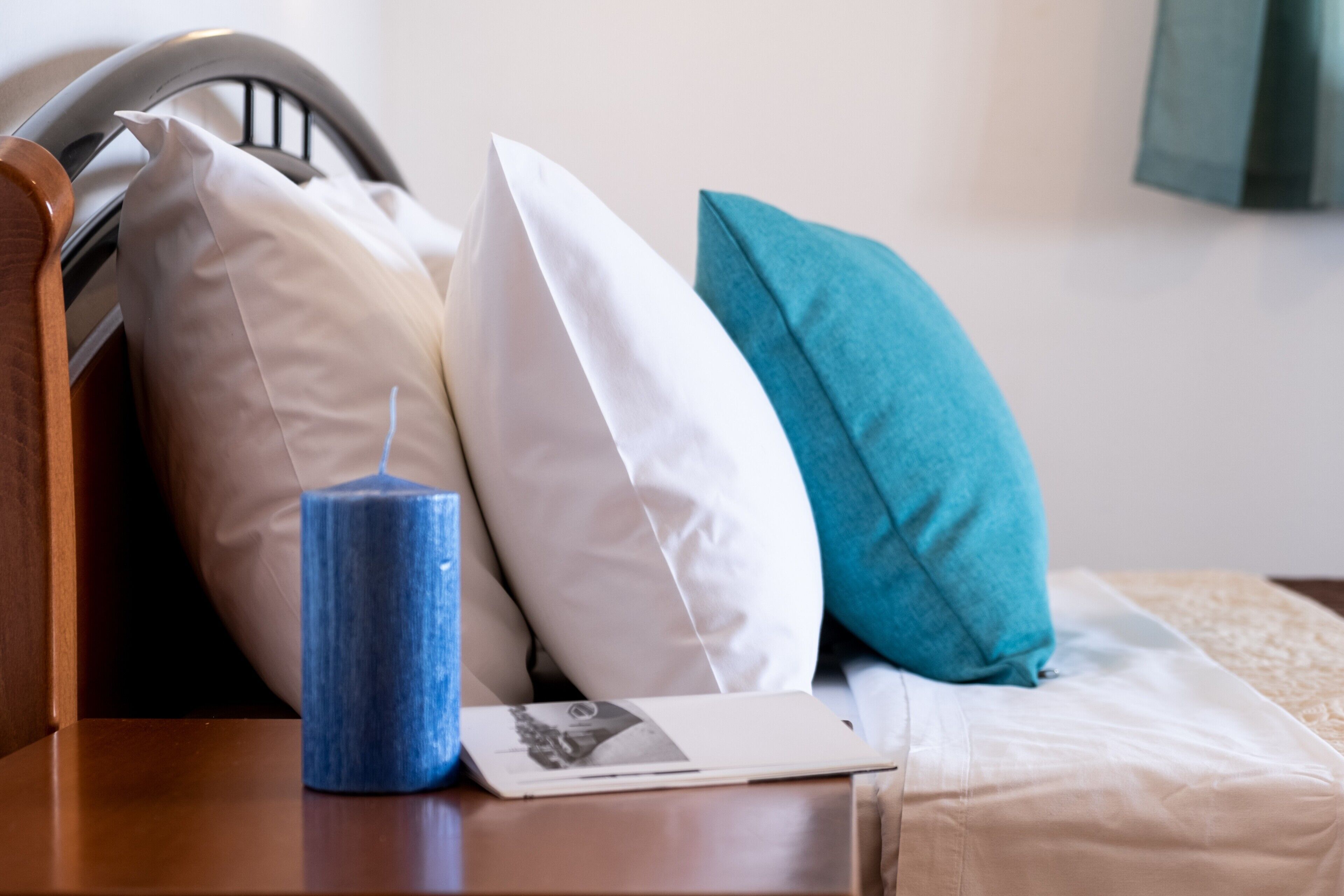 Een bed met kussens, een blauwe kaars en een fotoboek op een houten nachtkastje.