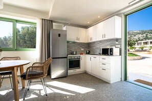 Une cuisine moderne avec des armoires blanches, un réfrigérateur en acier inoxydable, un four à micro-ondes et un four traditionnel. On y trouve une table à manger avec des chaises et une fenêtre avec des rideaux.