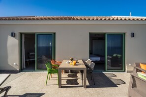 Un patio con una mesa y sillas, un gran ventanal corredizo y un techo de tejas.