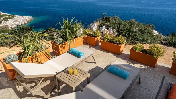 Eine Terrasse mit Sitzgelegenheiten im Freien, Blumentöpfen und Blick auf das Meer.
