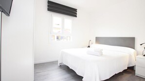 A bedroom with a bed, bedside tables, a TV, and a window with blinds. - Holiday Apartment "Rieres" with Terrace & Wi-Fi (PORT POLLENÇA)
