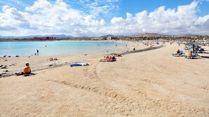 A beach with clear skies, people sunbathing, and a distant mountain range. - Vacation Home "Sol y Mar Caleta de Fuste" with Shared Pool, Garden & Wi-Fi (Caleta de Fuste)
