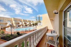 A hotel balcony with a pool, white railings, and a view of the pool area.