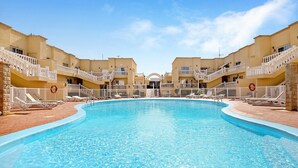 A swimming pool with white railings and lounge chairs, surrounded by beige buildings with balconies. - Vacation Home "Sol y Mar Caleta de Fuste" with Shared Pool, Garden & Wi-Fi (Caleta de Fuste)