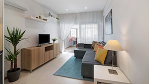 Un salon moderne avec un téléviseur à écran plat, un canapé avec des coussins, une table basse et une lampe.