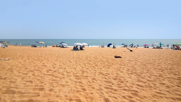 Une plage de sable avec des parasols et des gens.
