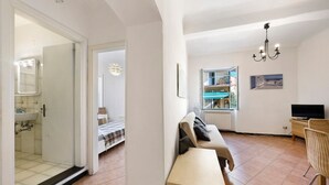 Ein modernes Wohnzimmer mit einer Couch, einem kleinen Tisch, einem Fernseher und einem Fenster mit Blick auf einen Balkon.