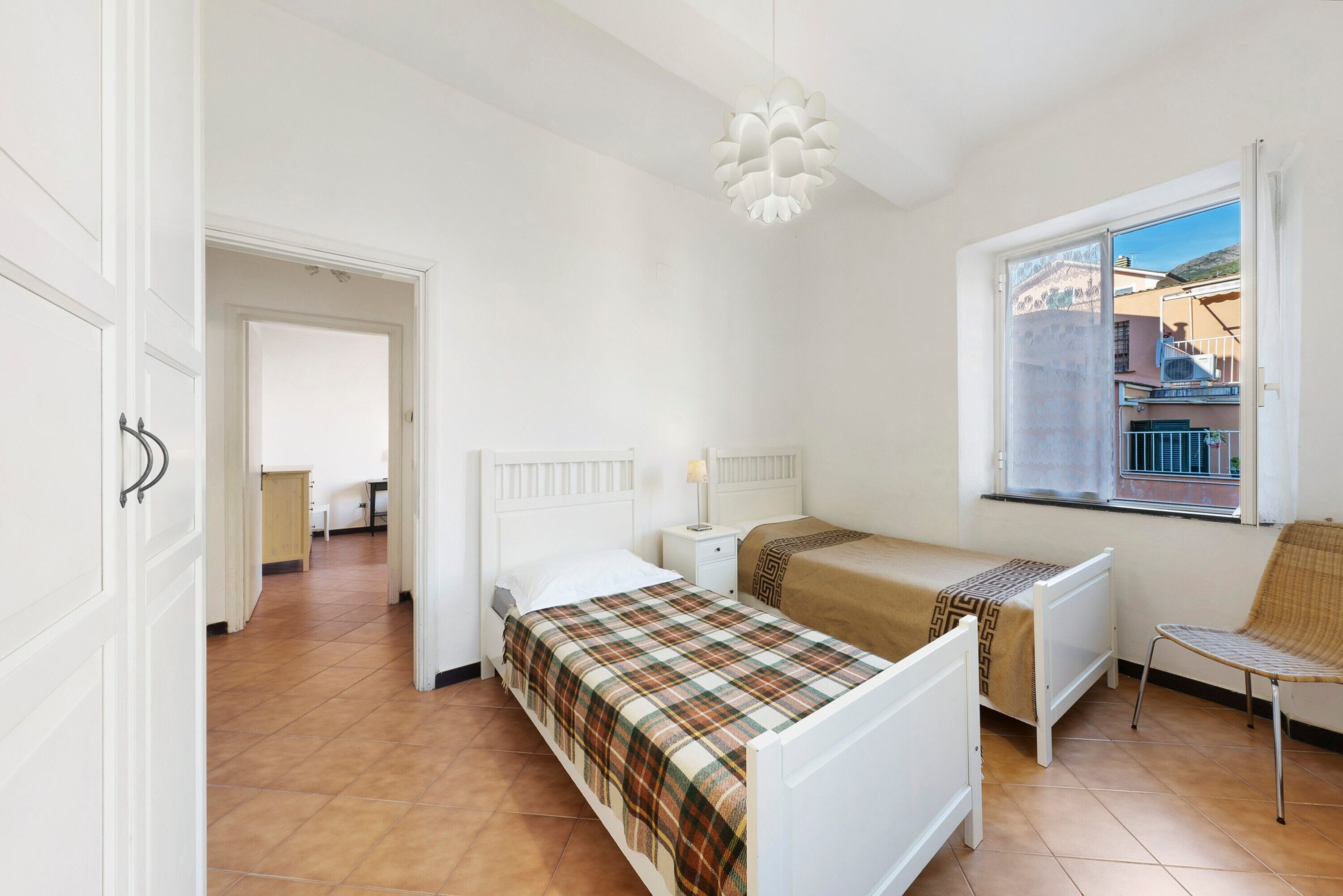 Une chambre avec deux lits, une fenêtre donnant sur un beau paysage, une chaise et un luminaire suspendu.