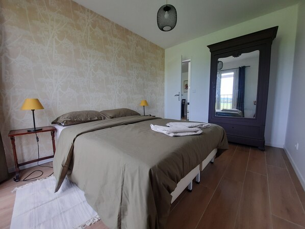 Una cama bien hecha con una colcha color crema, dos lámparas de noche y un espejo con marco oscuro.