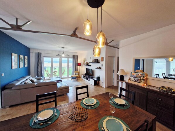 A modern living room with a sofa, dining table set for four, and a kitchen area with a TV and counter.