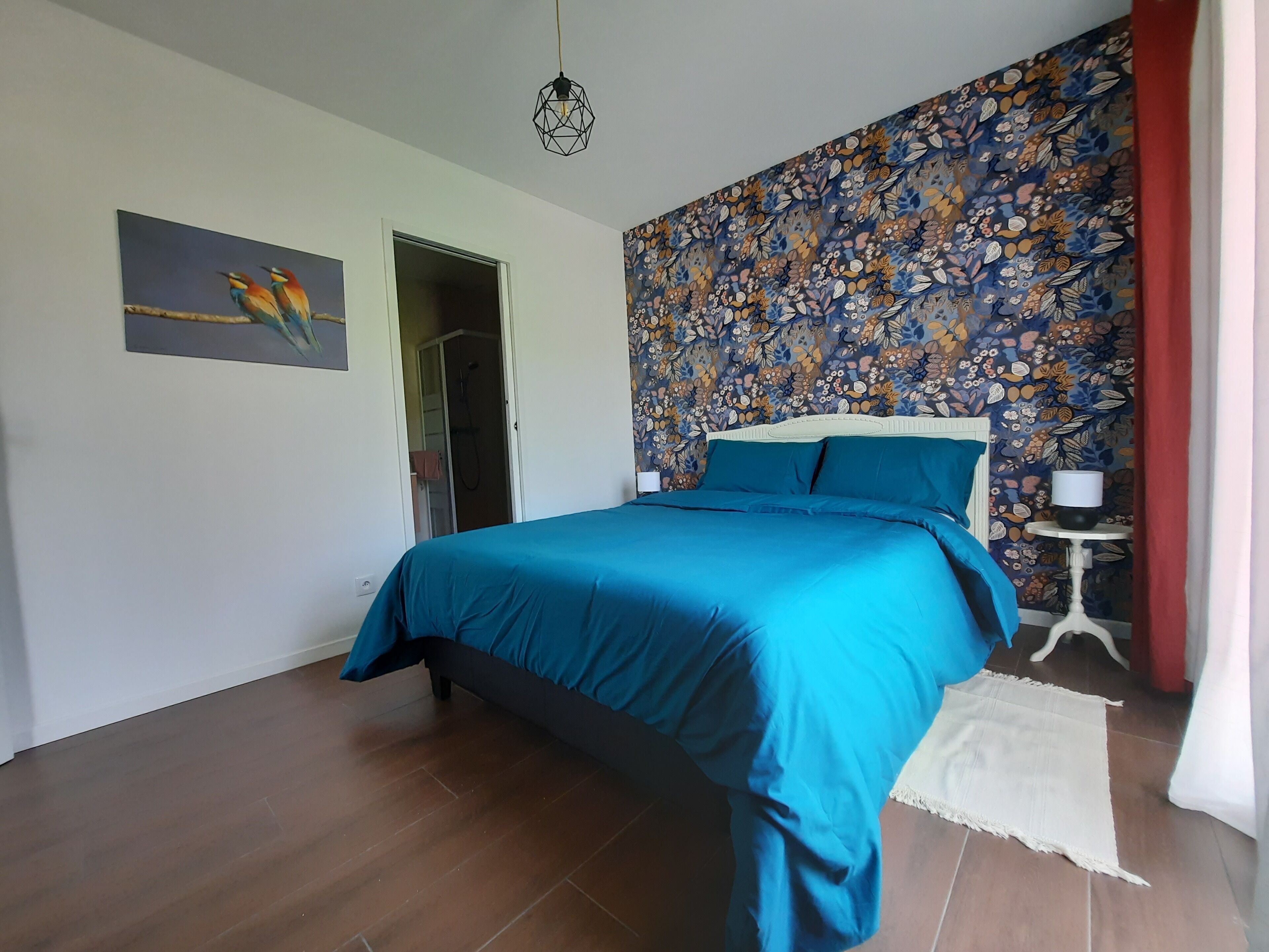 A bedroom with a bed, a shower, and a floral-patterned wall.