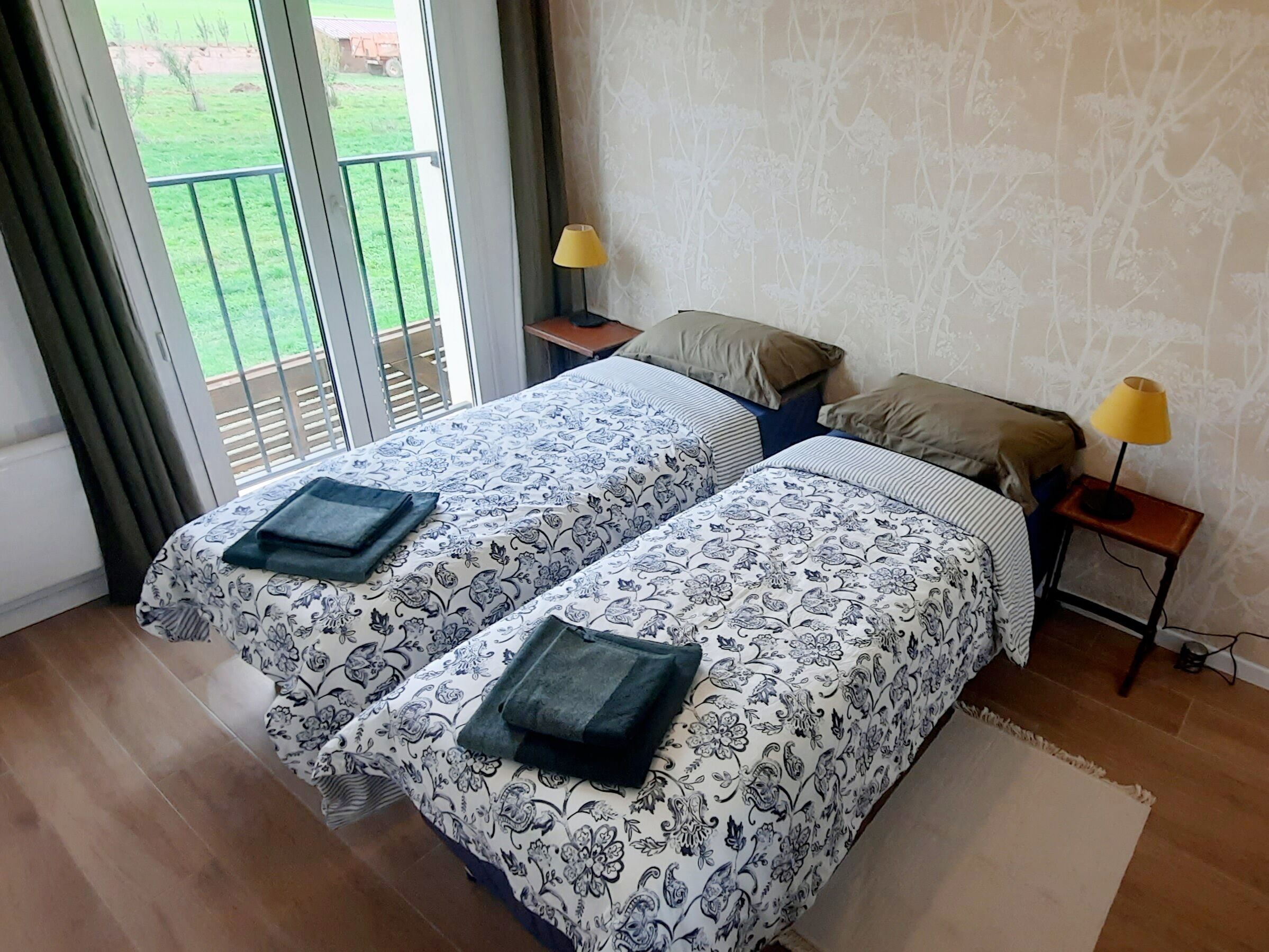 A bedroom with two beds, a sliding glass door to a balcony, and two bedside lamps.