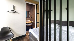 A modern hotel room with a bed, a chair, a bathroom with a sink and mirror, and a wardrobe. - Zandvoort Lodge 1 - Amazing couples getaway! (Zandvoort)