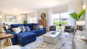A modern living room with a blue sectional sofa, a coffee table, and a dining area with chairs. - Casa da Boa Vida at Boa Vista Golf Resort, Bayview Village (Lagos)