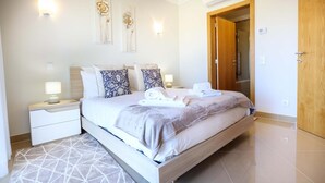A modern bedroom with a large bed, bedside tables, and a wooden door. - Casa da Boa Vida at Boa Vista Golf Resort, Bayview Village (Lagos)