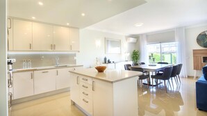 A modern kitchen with white cabinets, a central island, and a dining area with a table and chairs. - Casa da Boa Vida at Boa Vista Golf Resort, Bayview Village (Lagos)