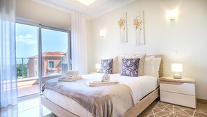 A hotel room with a large bed, a nightstand, a lamp, and a view of a building through the window. - Casa da Boa Vida at Boa Vista Golf Resort, Bayview Village (Lagos)