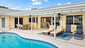 A poolside area with a covered patio, lounge chairs, and a dining table. - Luxurious Pool Home Central to Everything! (Palm Beach Gardens)