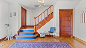A staircase with wooden steps and a blue riser, a wooden door, a chair with a blue cushion, and a chandelier. - BACKYARD WANDERLAND - Near ARK & Creation Museum - perfect for big families! (Burlington)