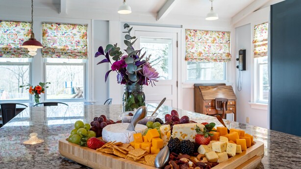 A marble countertop with a cheese and fruit platter, a vase with flowers, and a wooden sideboard. - BACKYARD WANDERLAND - Near ARK & Creation Museum - perfect for big families! (Burlington)