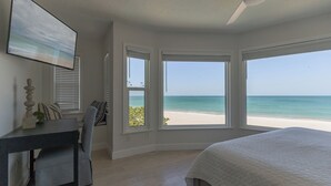 Un dormitorio con cama, escritorio y silla. Hay tres ventanas con vista a la playa.