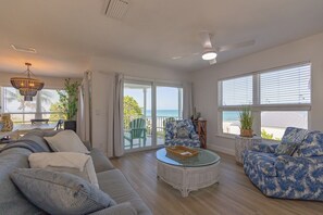 A spacious living room with a sofa, armchair, and coffee table, large windows with blinds, a ceiling fan, and a view of the outdoors. - Turtle Watch: *Gulf front *Heated Pool *Spectacular Views (Holmes Beach)