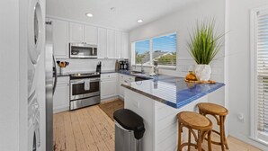 A modern kitchen with white cabinets, stainless steel appliances, a blue countertop, and a large window with blinds. - Turtle Beach: 2 Homes, Sleeps 10, Gulf Front with 2 Pools! (Holmes Beach)