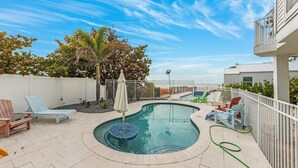 A swimming pool with lounge chairs and a small umbrella, surrounded by a white fence and trees. - Turtle Beach: 2 Homes, Sleeps 10, Gulf Front with 2 Pools! (Holmes Beach)