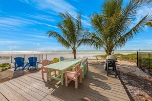 A wooden deck with a table and chairs, overlooking a beach with palm trees and the ocean. - Turtle Beach: 2 Homes, Sleeps 10, Gulf Front with 2 Pools! (Holmes Beach)