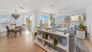 A spacious living area with a dining table, chairs, a sofa, and a TV mounted on the wall. - Turtle Beach: 2 Homes, Sleeps 10, Gulf Front with 2 Pools! (Holmes Beach)