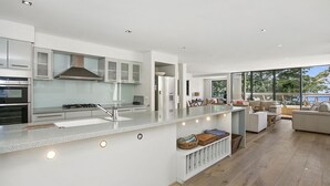 A modern kitchen with a central island, built-in appliances, and a dining area with a view. - Cetacea - Point Lonsdale (POINT LONSDALE)