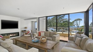 A spacious living room with a fireplace, comfortable seating, and large windows offering a view of the outdoors. - Cetacea - Point Lonsdale (POINT LONSDALE)