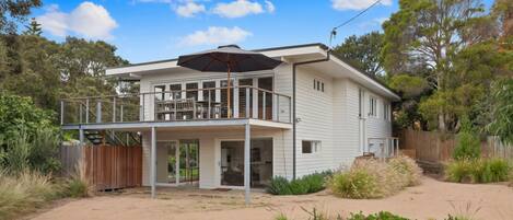 Ein zweistöckiges Haus mit Balkon, überdachter Terrasse und sandigem Garten.