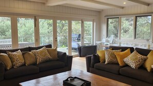 Amplia sala de estar con dos sofás oscuros, una mesa de centro de madera y grandes ventanas que ofrecen vistas al exterior.