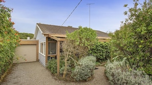 A small house with a tiled roof, a wooden porch, and a gravel driveway.