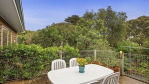A patio with a white table and chairs, surrounded by potted plants and a metal fence.