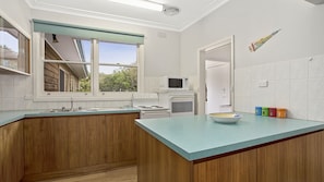 A kitchen with wooden cabinets, a teal countertop, a microwave, a stove, and a window with a view of greenery.