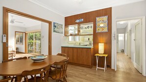 A dining area with a wooden table and chairs, a kitchen area with wooden cabinets, and a small stool with a lamp.