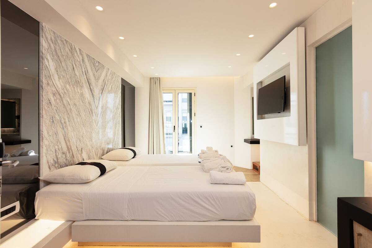Una habitación de hotel moderna con una cama grande, un televisor de pantalla plana montado en la pared y una pared decorativa de mármol.