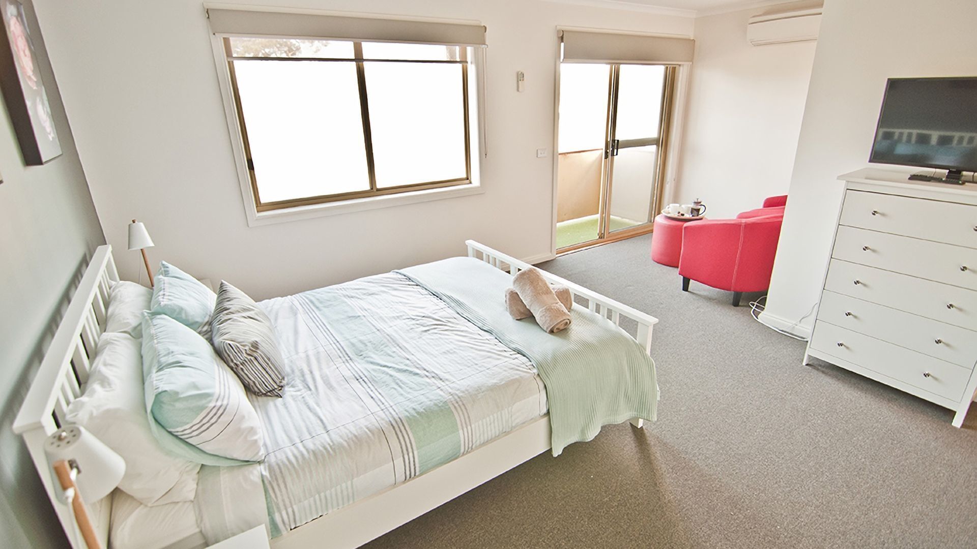 A bedroom with a bed, a dresser, a TV, and a red chair.